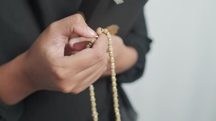 A person's hands hold a closed book and wooden prayer beads, emphasizing devotion. - Powered by Adobe