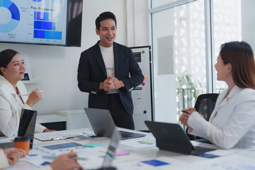 Asian businessman leading a meeting in a modern office, engaging team members in discussions about charts and statistics for collaborative decision-making