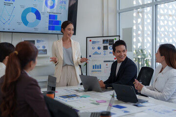 Asian businesswoman leading a meeting in a modern office, presenting data and engaging with her team as charts and graphs display on a large screen and whiteboard