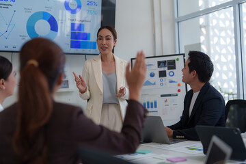 Asian businesswoman leads a meeting in a modern office, presenting data analysis and charts on a large screen, engaging with her team to discuss company performance and strategic planning