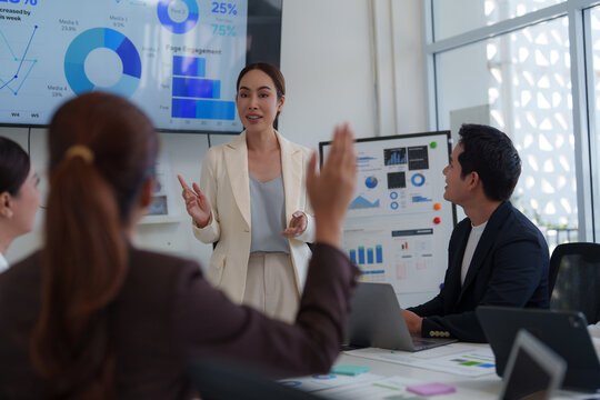 Asian businesswoman leads a meeting in a modern office, presenting data analysis and charts on a large screen, engaging with her team to discuss company performance and strategic planning