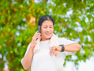 senior woman enjoying an outdoor workout, smiling while using mobile phone, smartwatch. Embracing...