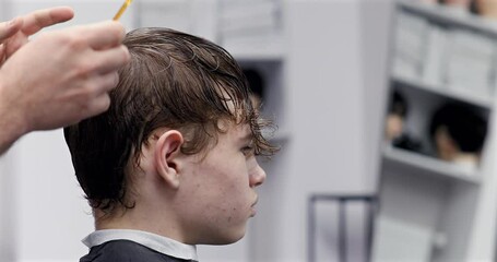 Professional hairdresser carefully separating hair sections, preparing for precise cutting technique in stylish salon