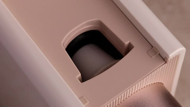 Close-up of woman's hand inserts a plastic recyclable coffee capsule with a paper lid into a capsule coffee machine in pale beige, champagne or rose gold. Kitchen appliances