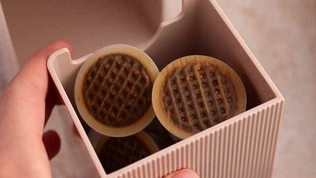 A woman's hand shows the compartment for used capsules from a capsule coffee machine in pale beige, champagne or rose gold. Recyclable plastic coffee capsules with a paper lid