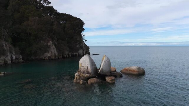 Split Apple Rock at tasman bay. during sunny day with clouds. Aerial orbit. Exploring New Zealand. Rocky coastline with trees and ocean water in background.