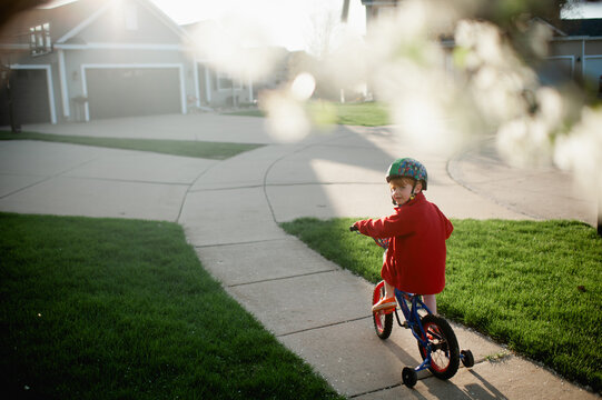 Boy with helmet on rides bike with training wheels down sidewalk