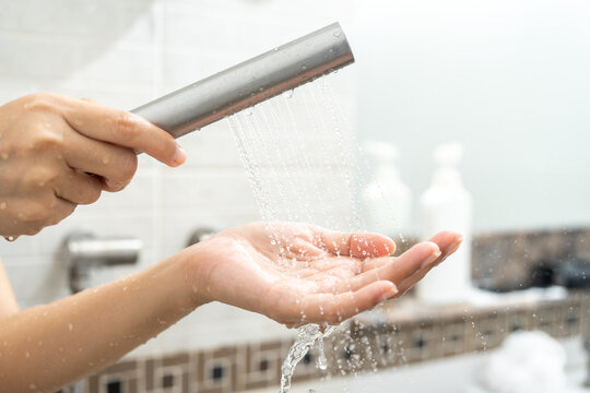 Young woman useing hands to test the water temperature when taking a shower. Hands female touches the water from the shower with her hands.