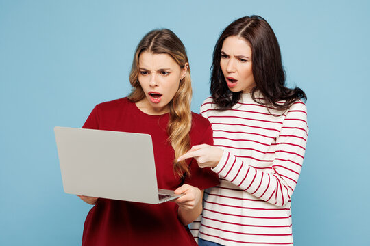 Young shocked IT couple two friends women wearing red casual clothes together hold use work point finger on laptop pc computer isolated on pastel plain light blue cyan background. Lifestyle concept.