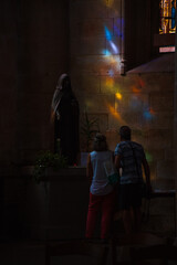Mid aged couple praying to saint (back view; unrecognizable) in church. Colorful spots of sunlight...