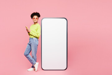Full body side view young woman she wear green sweater casual clothes big huge blank screen mobile cell phone with workspace area using smartphone isolated on plain pink background. Lifestyle concept.