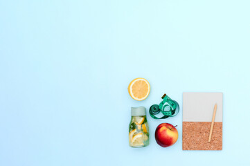 Transport yourself to a sustainable paradise with this image of an eco-friendly notebook and pen, apple and orange, roulette, presented alongside a bottle of lemonade flat lay