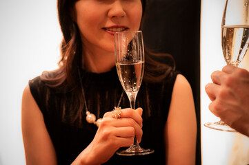 A woman in a sleeveless black dress smiles while holding a champagne glass at an upscale bar. The warm lighting and her elegant accessories convey a festive, celebratory mood.
Keywords: