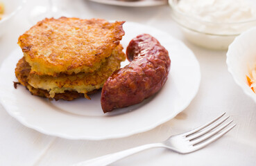 Potato pancakes with fried sausage on white plate