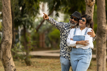 Indian happy middle aged lovely couple pointing finger or hand to side way Asian husband and wife relaxing at park spend time together, relationship and people concept.