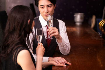 A couple dressed in formal attire clinks champagne glasses in a warm, romantic bar setting. Their smiles reflect joy and connection, emphasizing a mood of celebration.