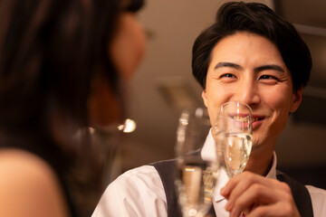 Close-up of a smiling man in a white shirt and vest holding a champagne glass, sharing an intimate moment during a romantic evening date at a stylish bar.