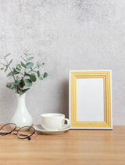 Eucalyptus branches, coffee cup, eyeglasses and empty photo frame creating cozy atmosphere on table