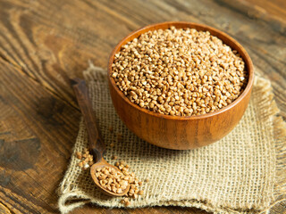 Organic buckwheat groats in a wooden bowl with a spoon on a linen napkin on a wooden table.