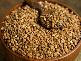 Organic buckwheat groats in a wooden bowl with a spoon on a linen napkin on a wooden table.