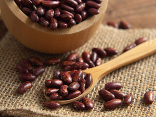 Red kidney beans in a scoop on a wooden table against a white background.