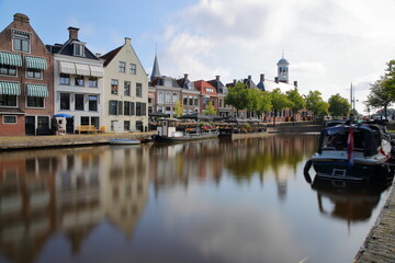 Naklejka premium Reflections of traditional houses, barges and boats on the little canal (klein Diep) in Dokkum, Friesland, Netherlands, with the Oud Stadhuis (Old Town Hall, built in 1610) in the background