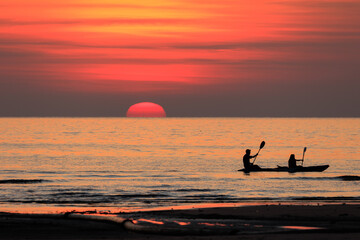 A couple paddle boats in the ocean at sunset