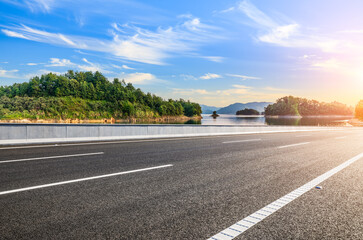 Fototapeta premium Empty asphalt road with beautiful lake and mountain at sunset