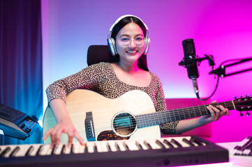 Asian teen girl playing guitar, composing music in home recording studio, LED lighting, at night...