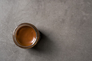 Top view of chocolate spread or nougat cream with hazelnuts in glass jar on dark background