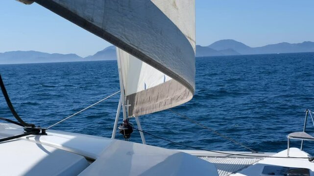 sailing unser sail on bord ov multihull white catamaran, waves, blue water, sunny perfect day, mountains on background
