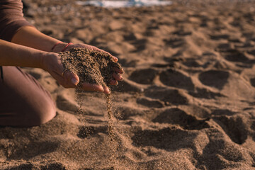 Person holding sand with hands on a beach during sunlight in a calm environment