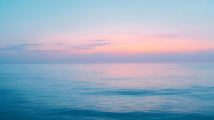 Obraz premium Gentle pink and peach sunrise hues reflecting softly on calm blue ocean water under a serene pastel blue sky with subtle clouds, creating a peaceful and warm morning seascape