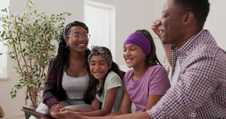 The family sits on the couch in their apartment during renovation, browsing a tablet for paint colors. Dad shows suggestions, and mom is surprised by the choices.