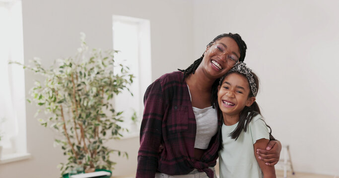 Two sisters share a warm hug and joyful smiles as they look at the camera. They are resting after painting the walls during a home renovation.