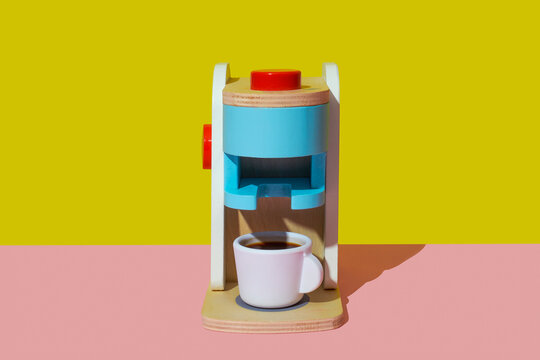 Toy coffee maker with a cup of coffee on a pink background