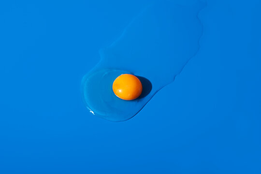 Raw egg yolk and egg white scattered on a blue surface in a studio setting