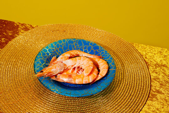 Cooked prawns on a blue glass plate with a golden velvet tablecloth in a studio setting