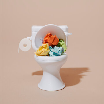 Toy toilet with colorful crumpled paper balls on a beige background