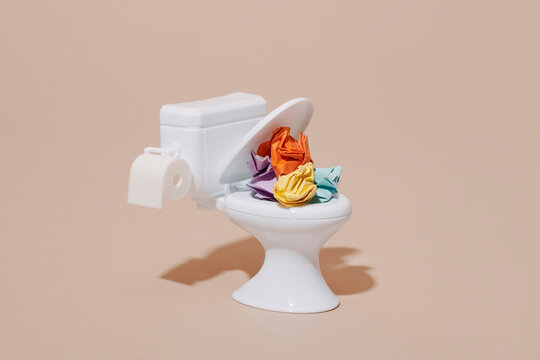 Toy toilet with colorful crumpled paper balls on a beige background