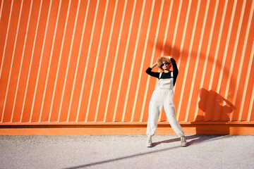 Woman with curly afro hairstyle dancing happily in front of an orange wall