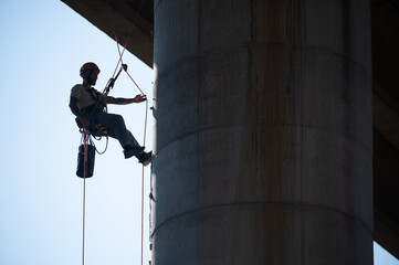 Rope access technician securing himself with a rope on concrete bridge pillar