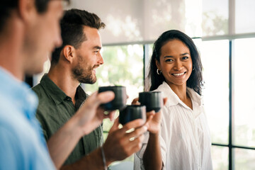 Happy creative diverse colleagues having fun while talking and drinking coffee, tea in working break