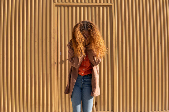 Young woman covering face with hands in front of metal wall