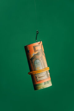 Rolled euro banknote on a hook against a green background symbolizing easy money and financial traps