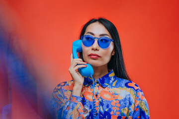 Woman with blue sunglasses and phone against an orange background