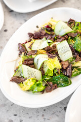 Fresh salad with mixed greens, cucumbers, and grilled meat on a white plate. Bright and appetizing, perfect for healthy dining or culinary presentations