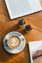 A latte and potted succulents on a wooden table alongside a minimalist white-cover magazine, radiating cozy charm.