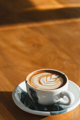 A ceramic cup with latte art on a wooden table, illuminated by sunlight.