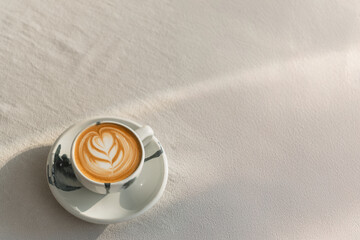 A latte with heart-shaped art on a ceramic cup, bathed in soft sunlight.